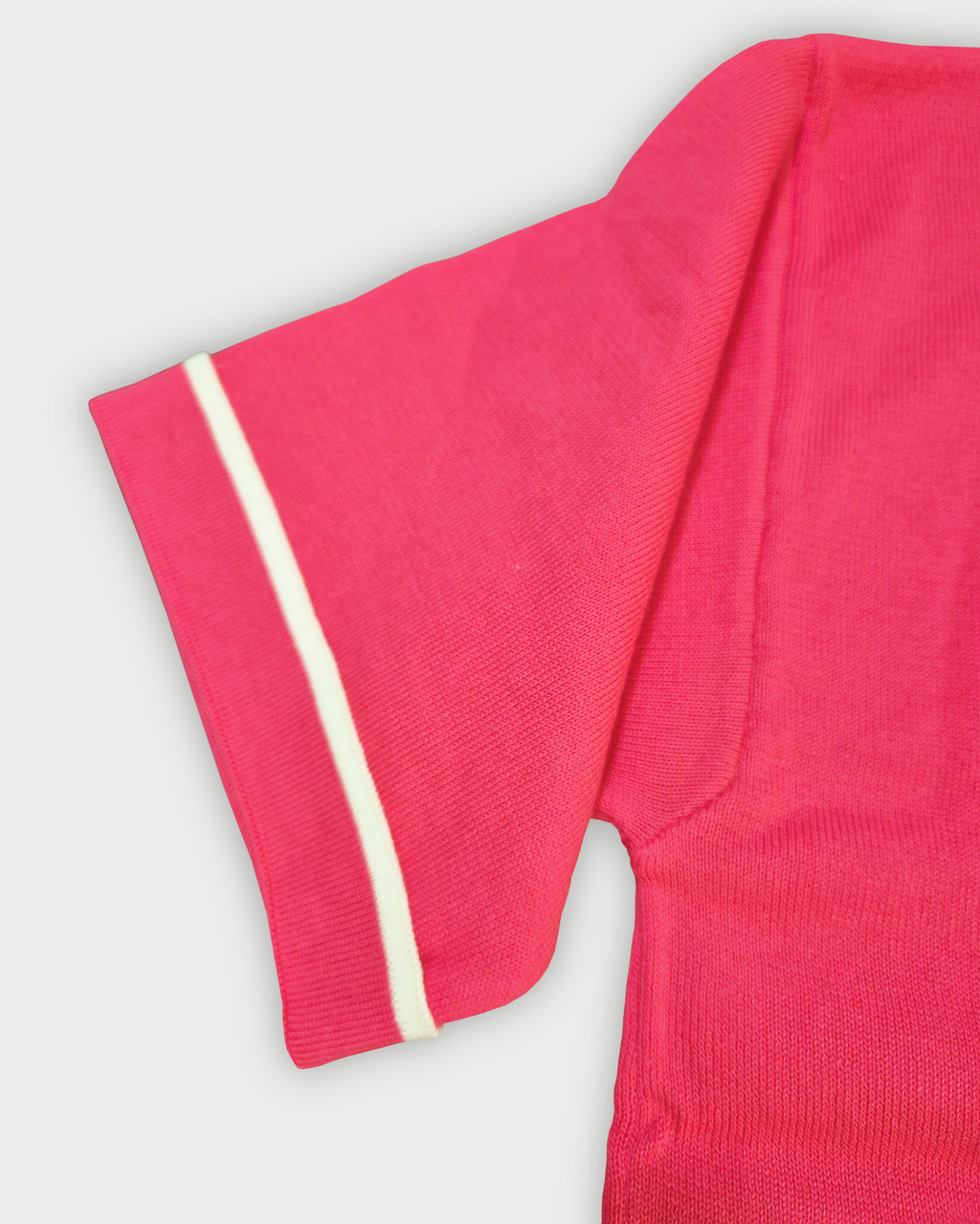 Dettaglio della manica con bordino bianco della polo donna over in maglia di cotone rosa corallo con colletto e bordi bianchi su sfondo bianco