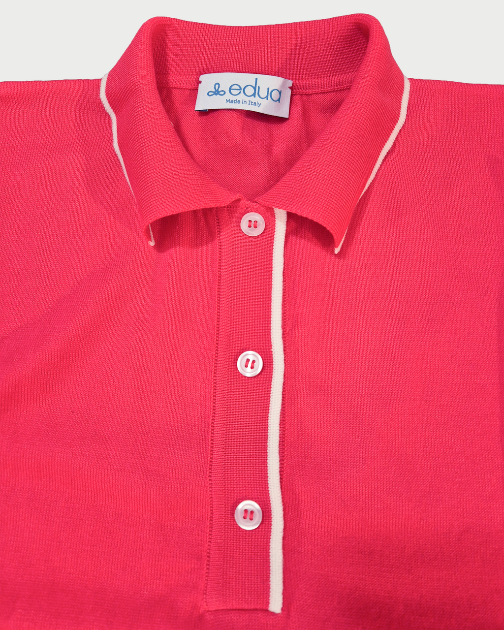 Dettaglio della polo donna over in maglia di cotone rosa corallo con colletto e bordi bianchi su sfondo bianco