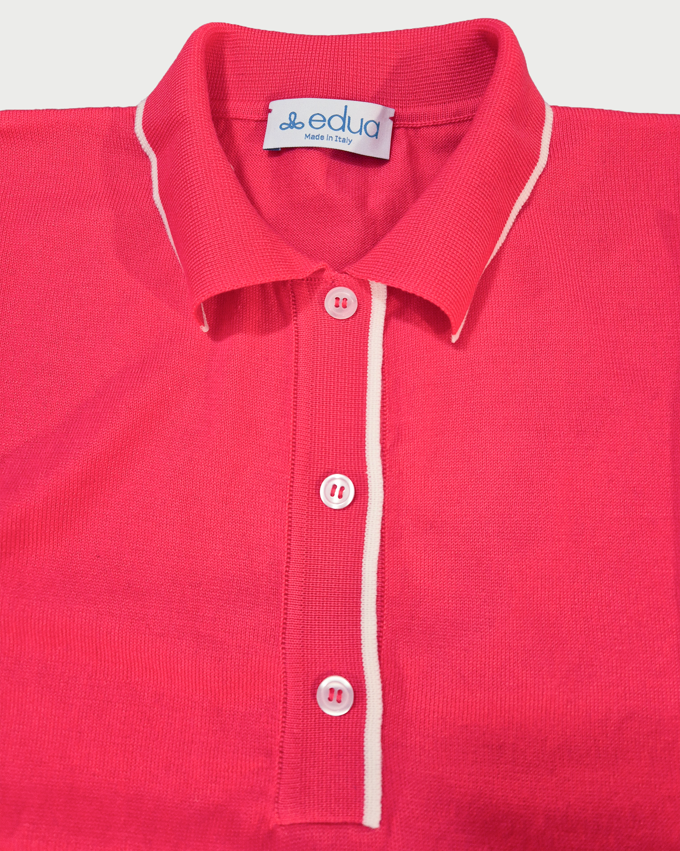 Dettaglio della polo donna over in maglia di cotone rosa corallo con colletto e bordi bianchi su sfondo bianco