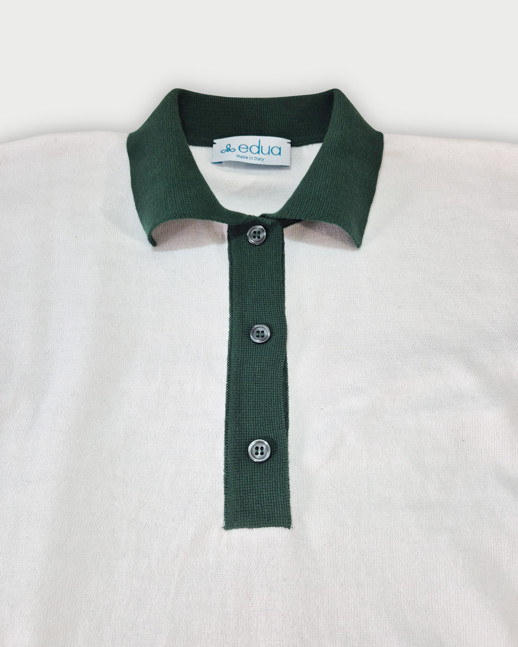 Dettaglio del colletto verde della polo donna over in maglia di cotone bianca su sfondo bianco