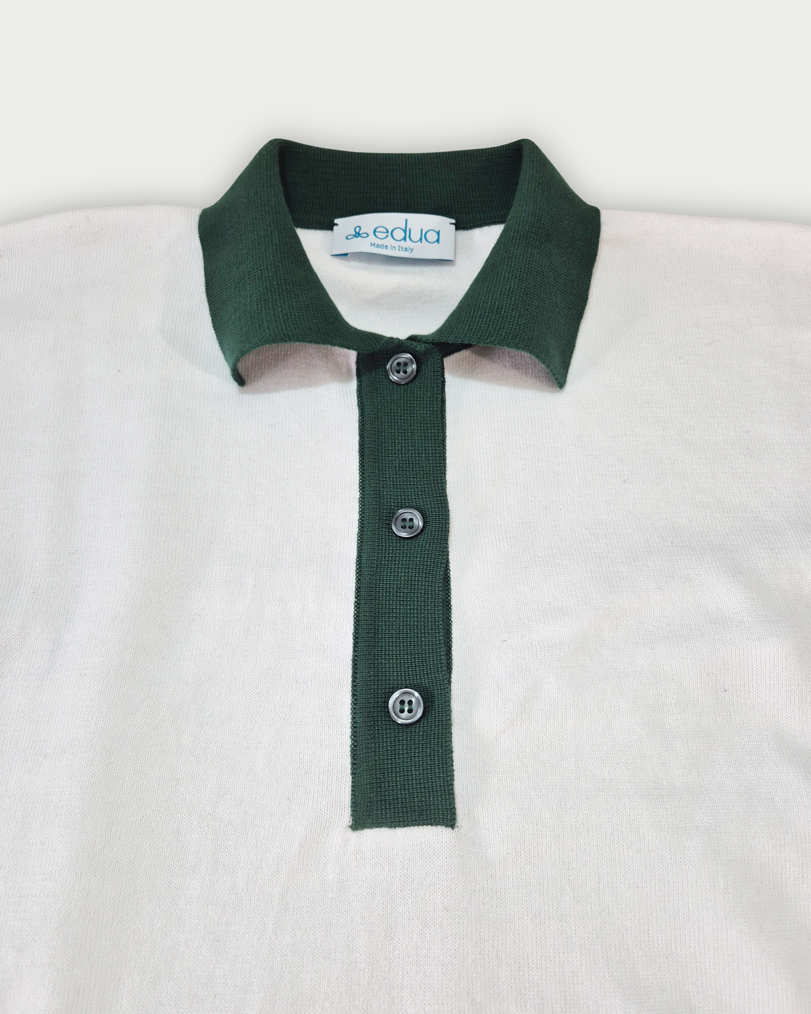 Dettaglio del colletto verde della polo donna over in maglia di cotone bianca su sfondo bianco
