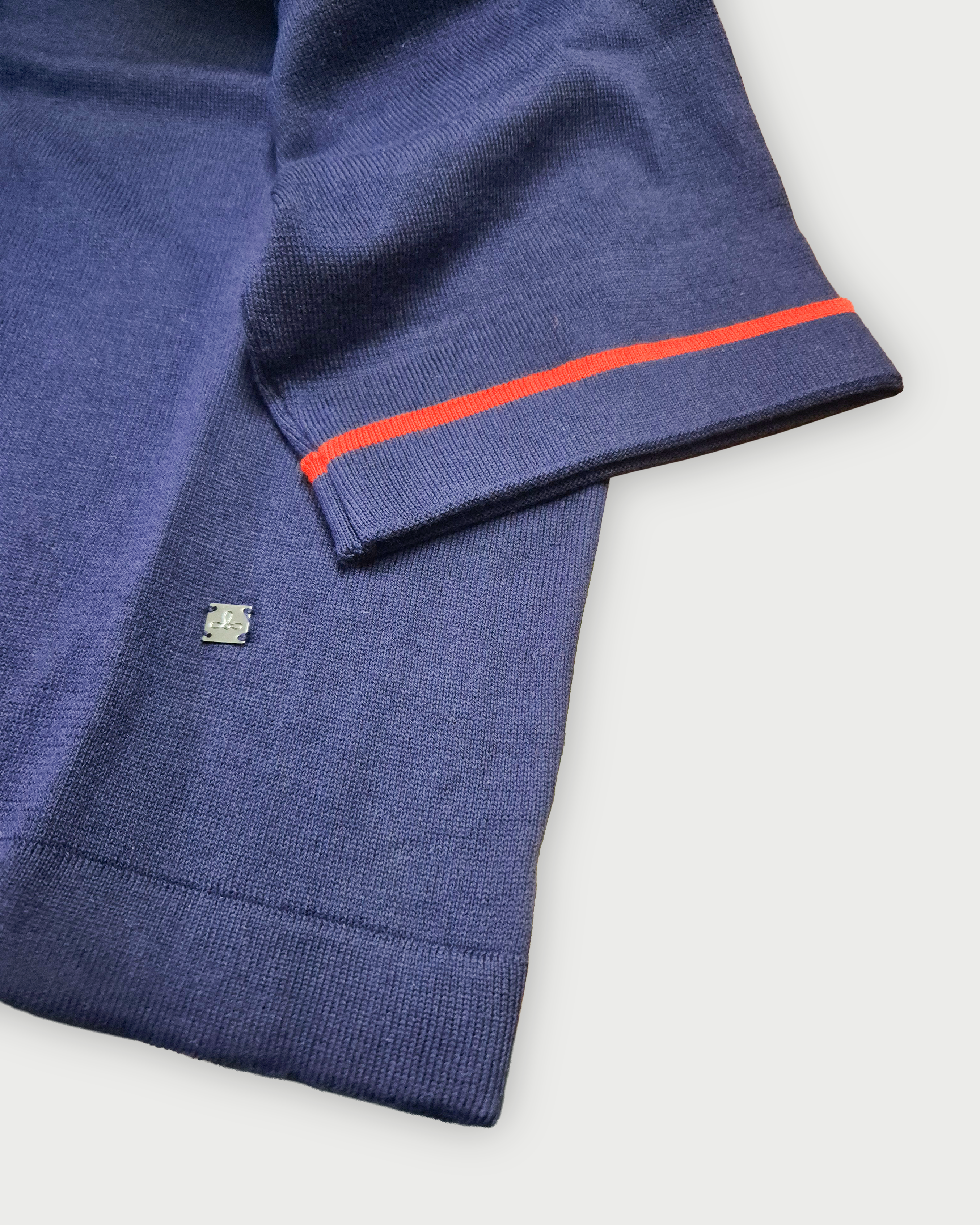 Dettaglio della manica con bordino rosso e logo Edua sul fondo della maglia donna in maglia di cotone blu con girocollo su sfondo bianco