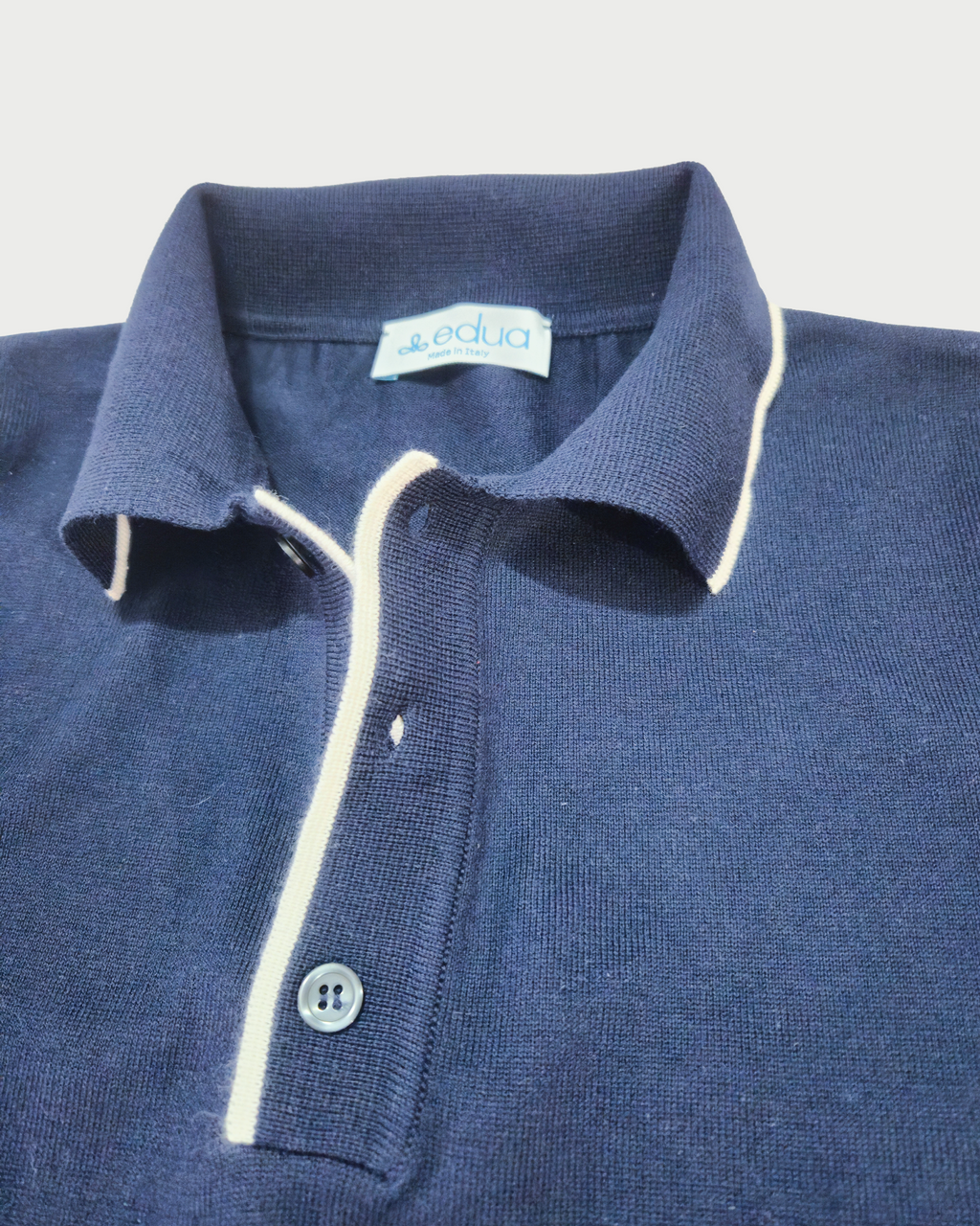 Dettaglio colletto polo maniche lunghe uomo in maglia di cotone blu su sfondo bianco
