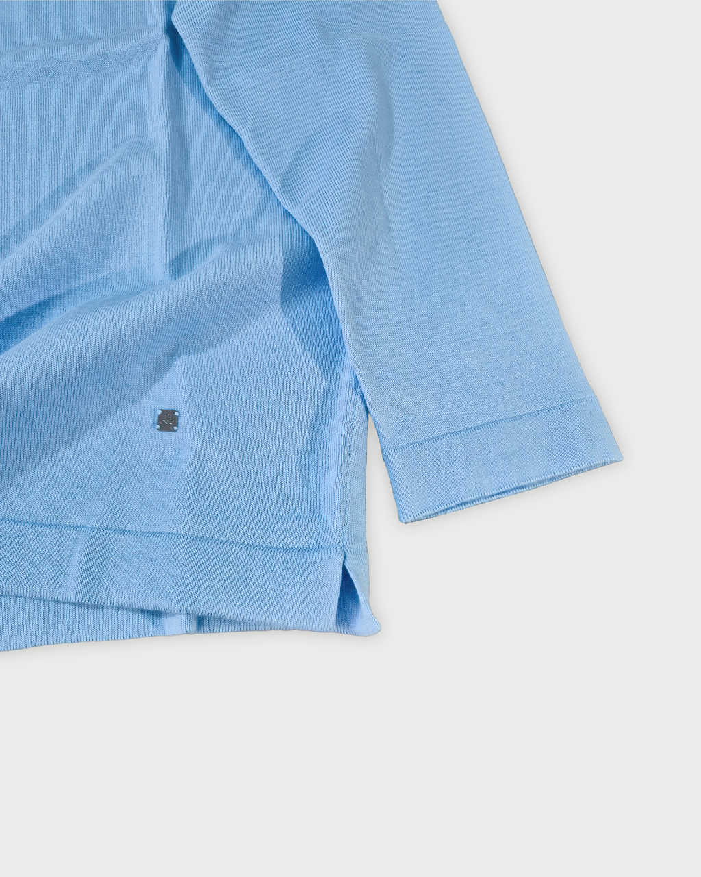 Dettaglio manica e fondo polo maniche lunghe uomo in maglia di cotone celeste su sfondo bianco