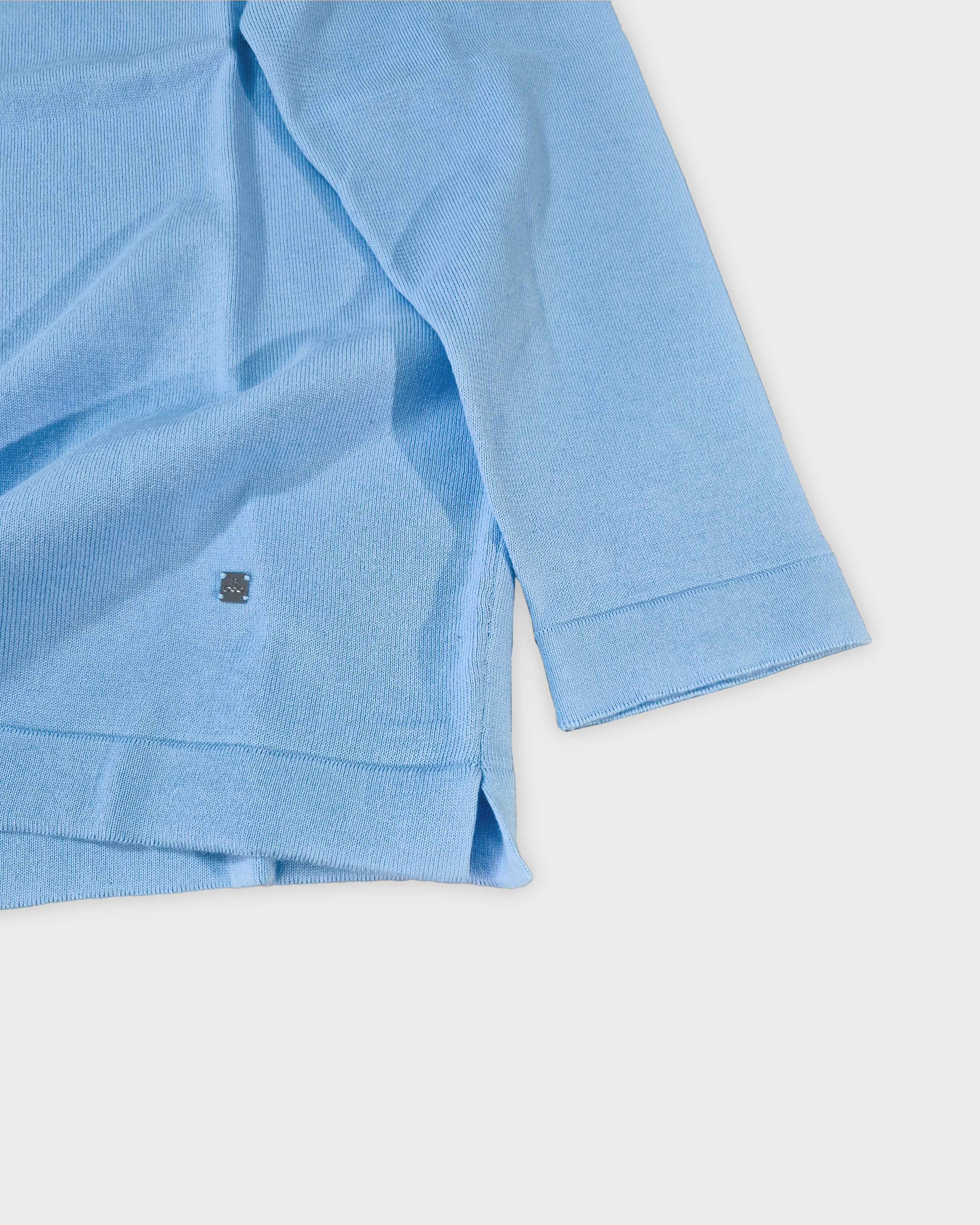 Dettaglio manica e fondo polo maniche lunghe uomo in maglia di cotone celeste su sfondo bianco