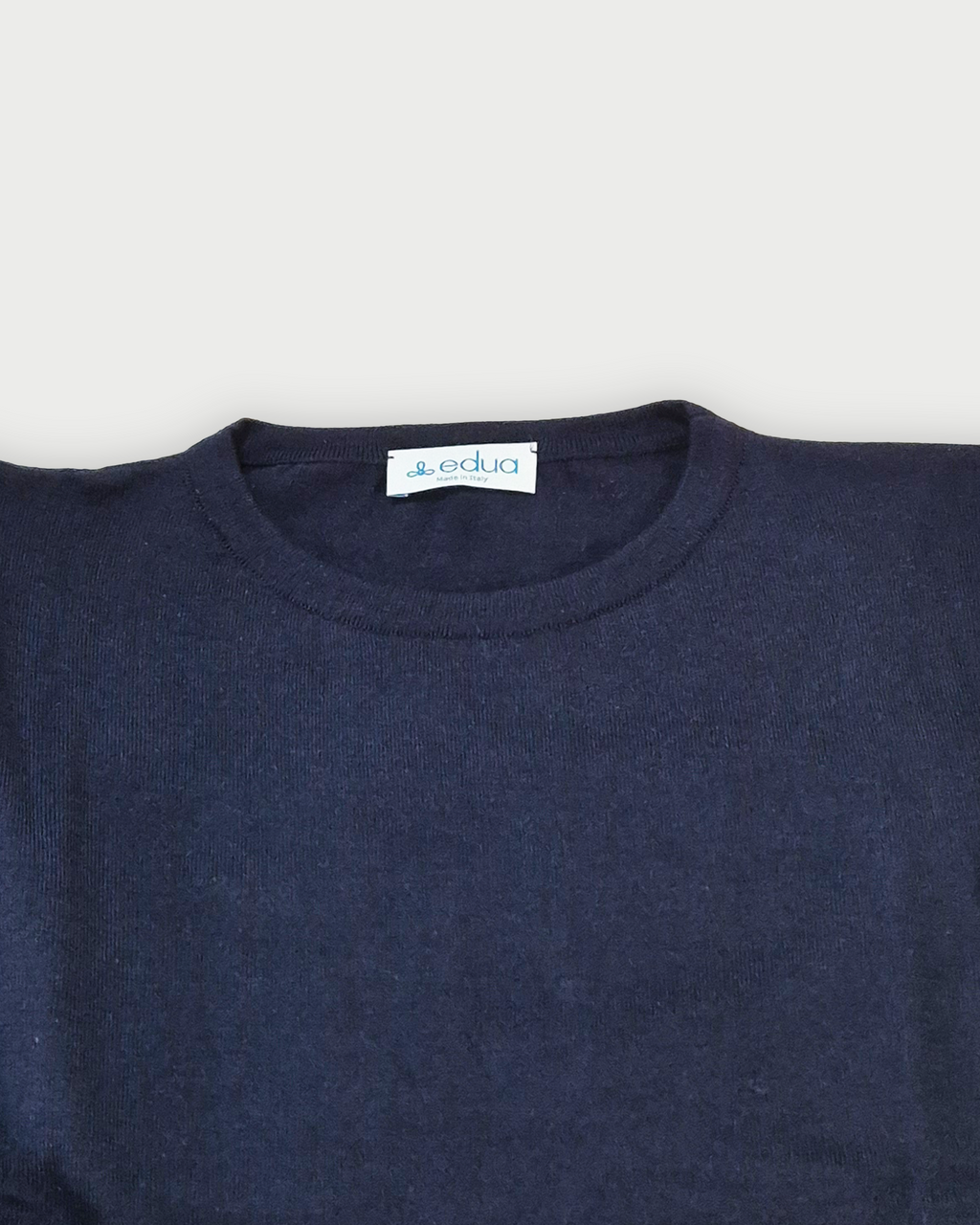 Dettaglio del colletto della maglia donna in maglia di cotone blu con girocollo e profili rossi sulle maniche su sfondo bianco