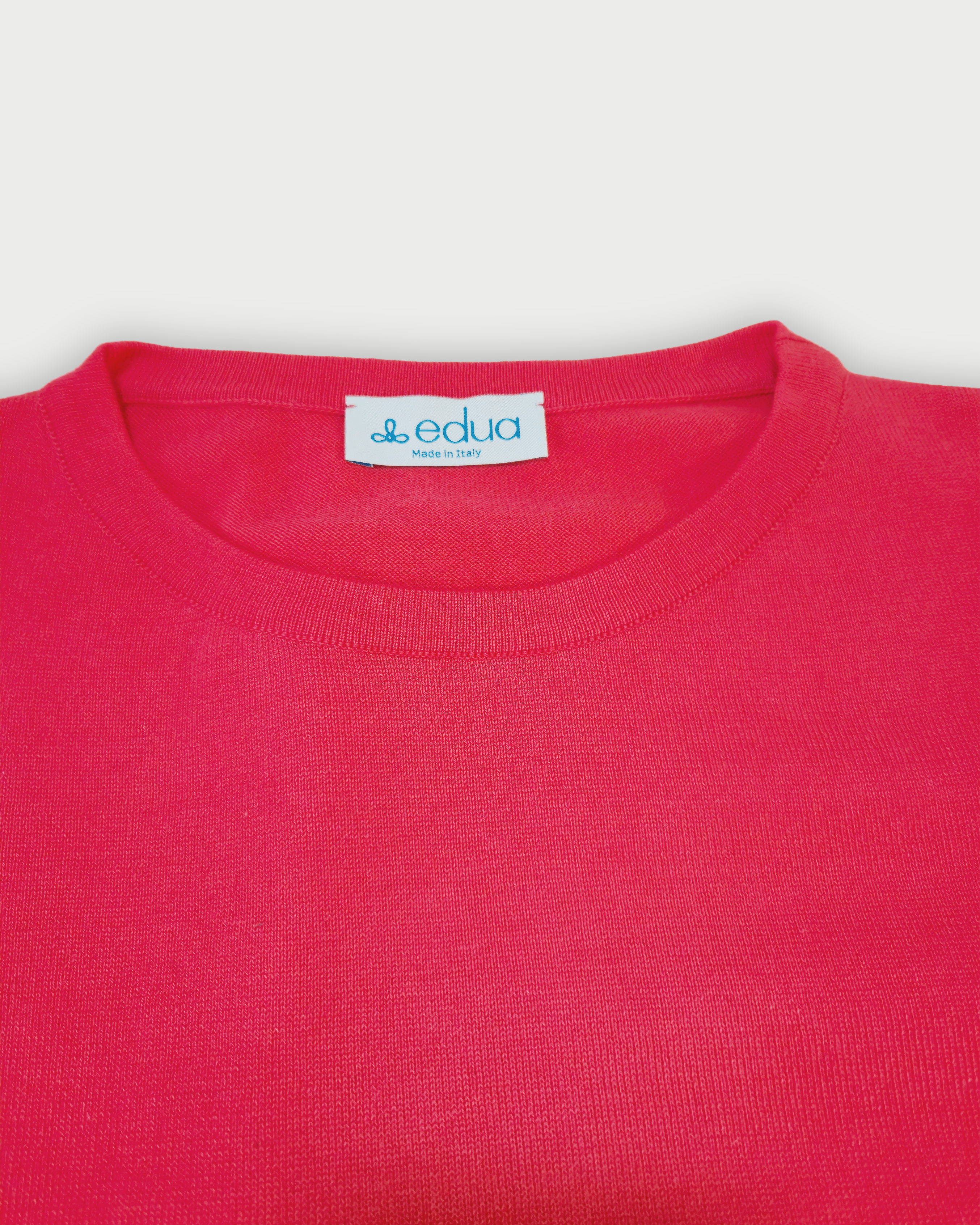 Dettaglio del colletto della maglia donna in maglia di cotone rosa corallo con girocollo e profili bianchi sulle maniche su sfondo bianco