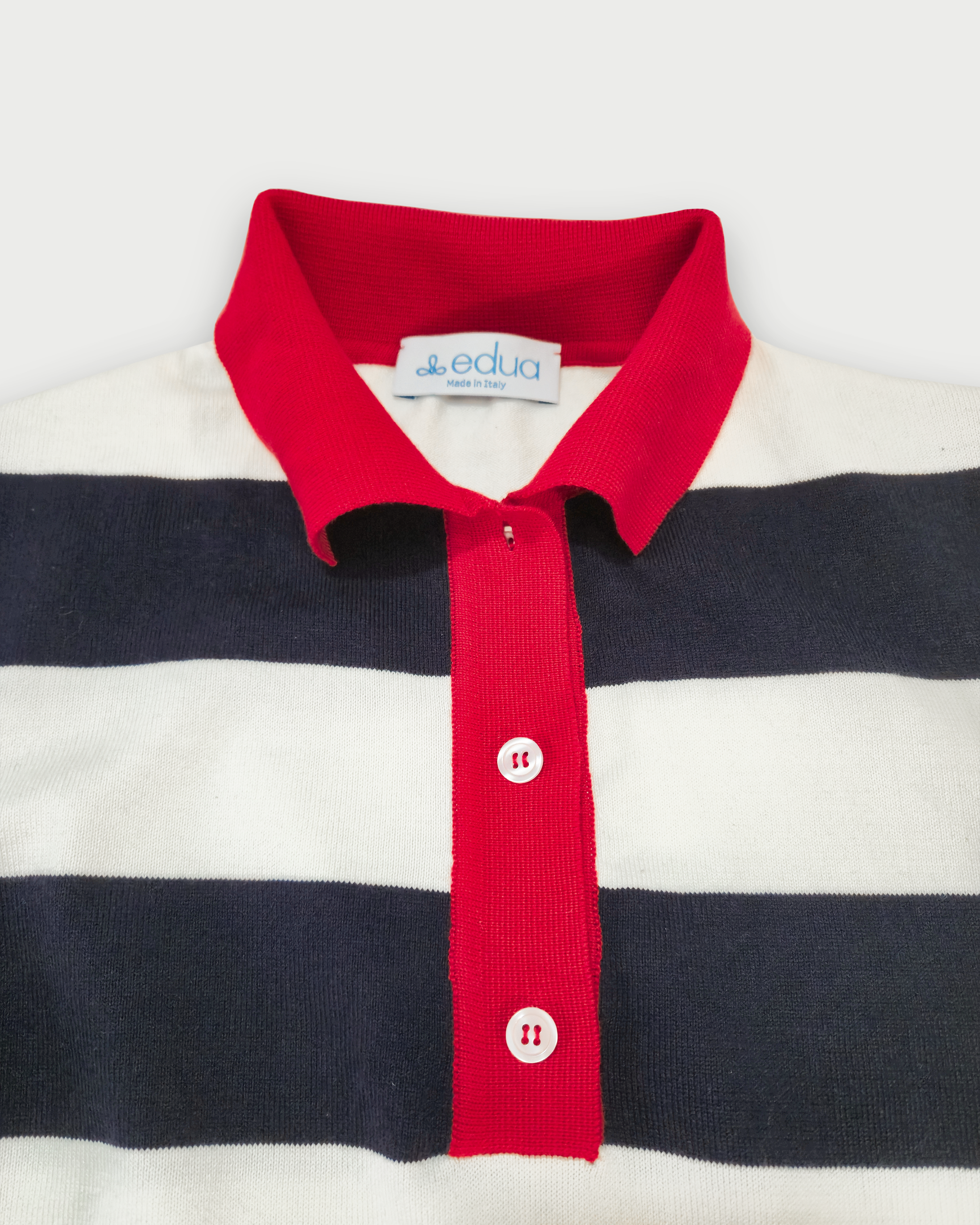 Dettaglio del colletto rosso e dell’abbottonatura della polo donna a righe blu e bianche in maglia di cotone
